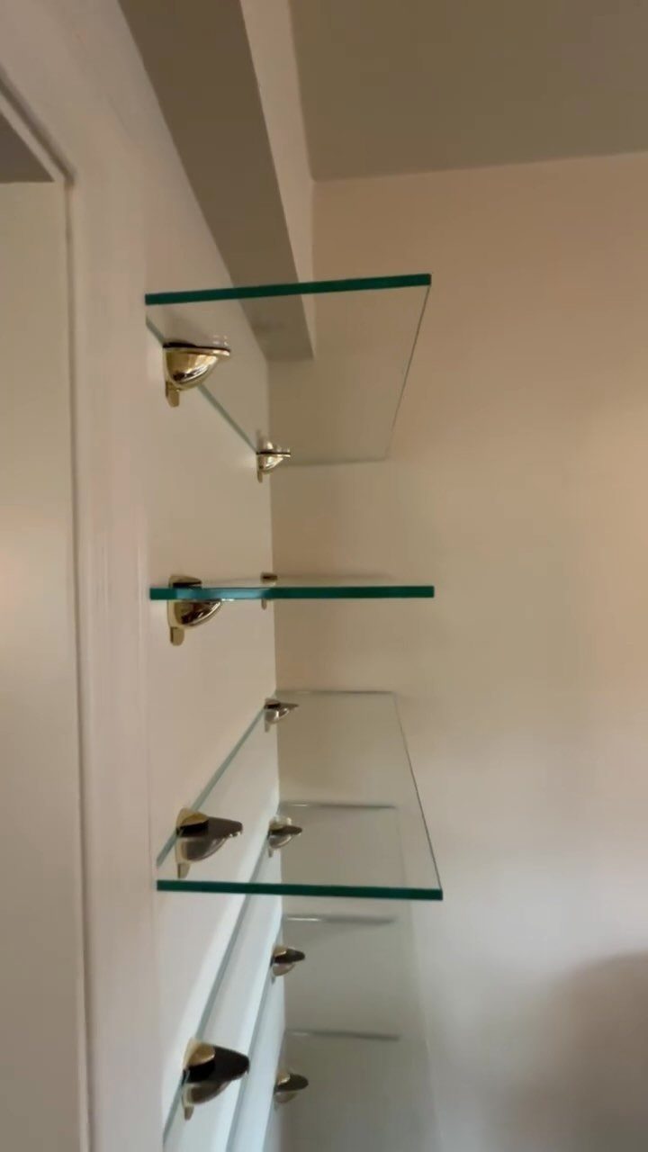 Glass shelves with gold brackets mounted on a plain white wall.