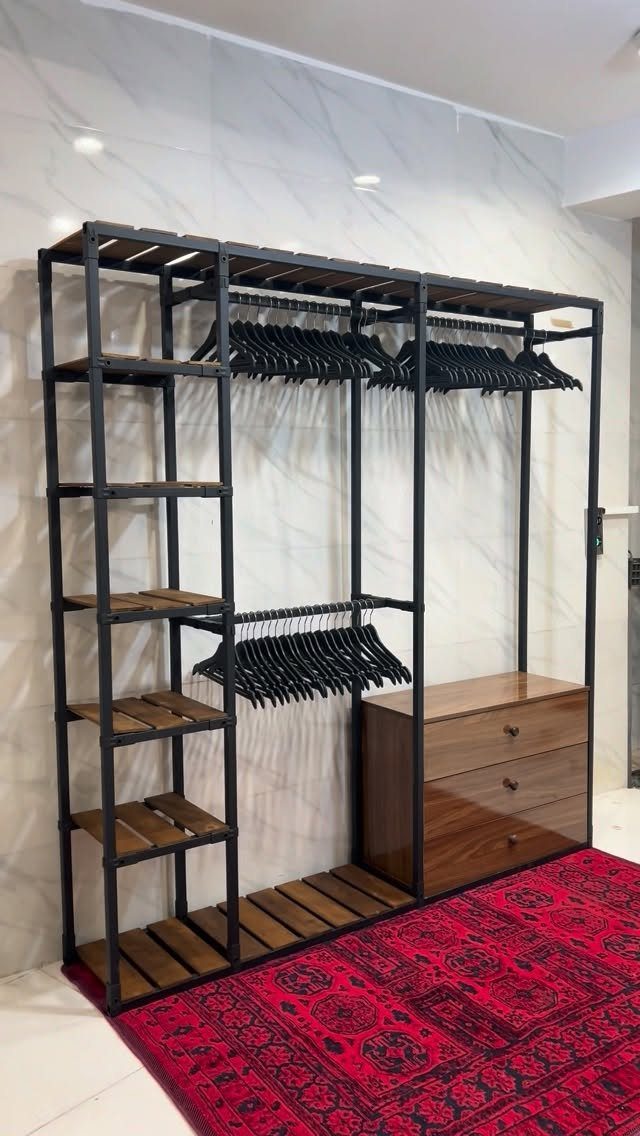 Industrial open wardrobe with black metal frames, wooden shelves, and a brown dresser.