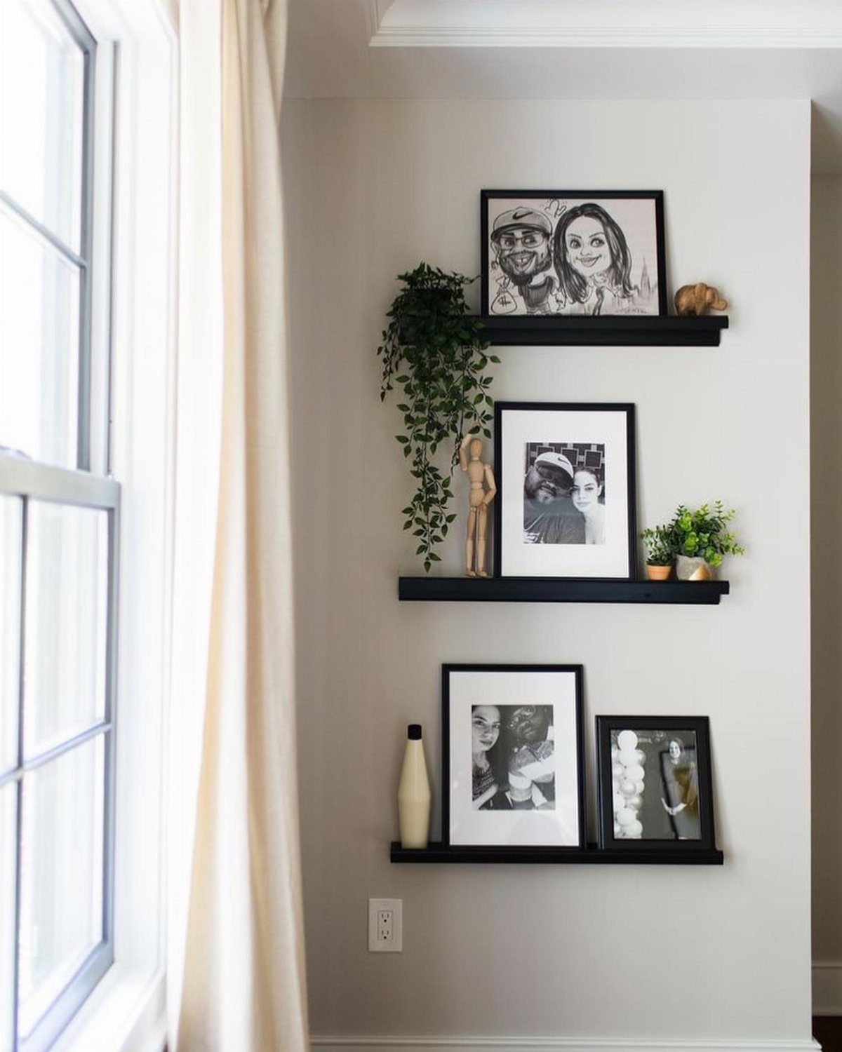 Black picture ledge shelves holding framed photos and small green plants on a wall.