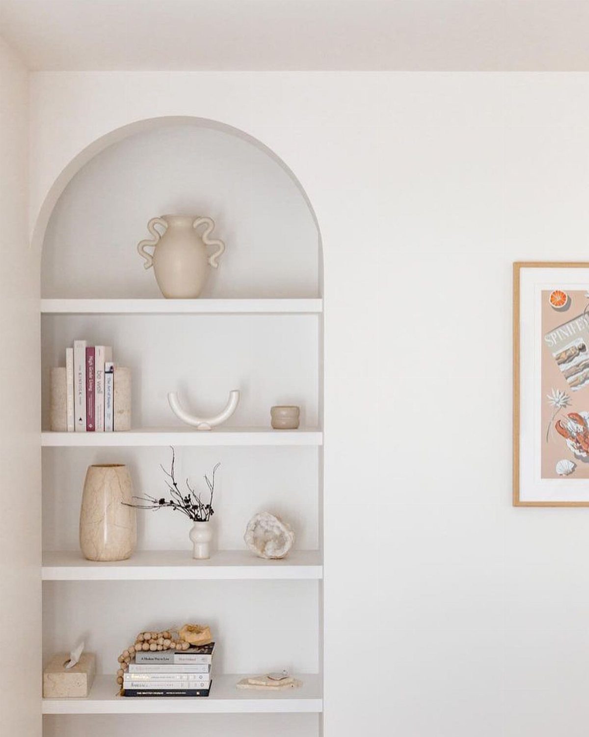 Arched recessed wall shelf with white paint holding vases, books, and decorative objects.