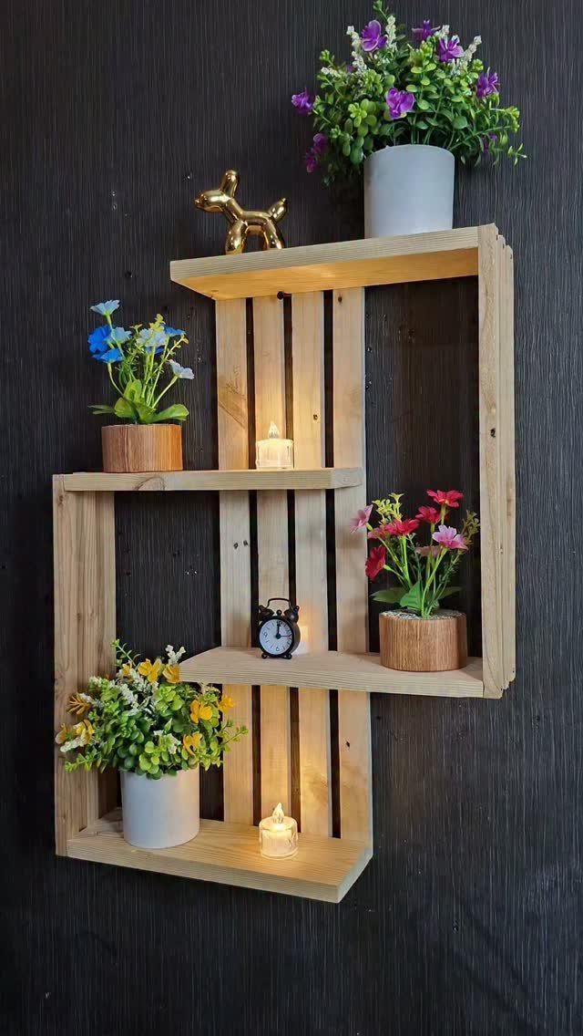 Wooden pallet wall shelf with potted flowers, candles, and a small alarm clock.
