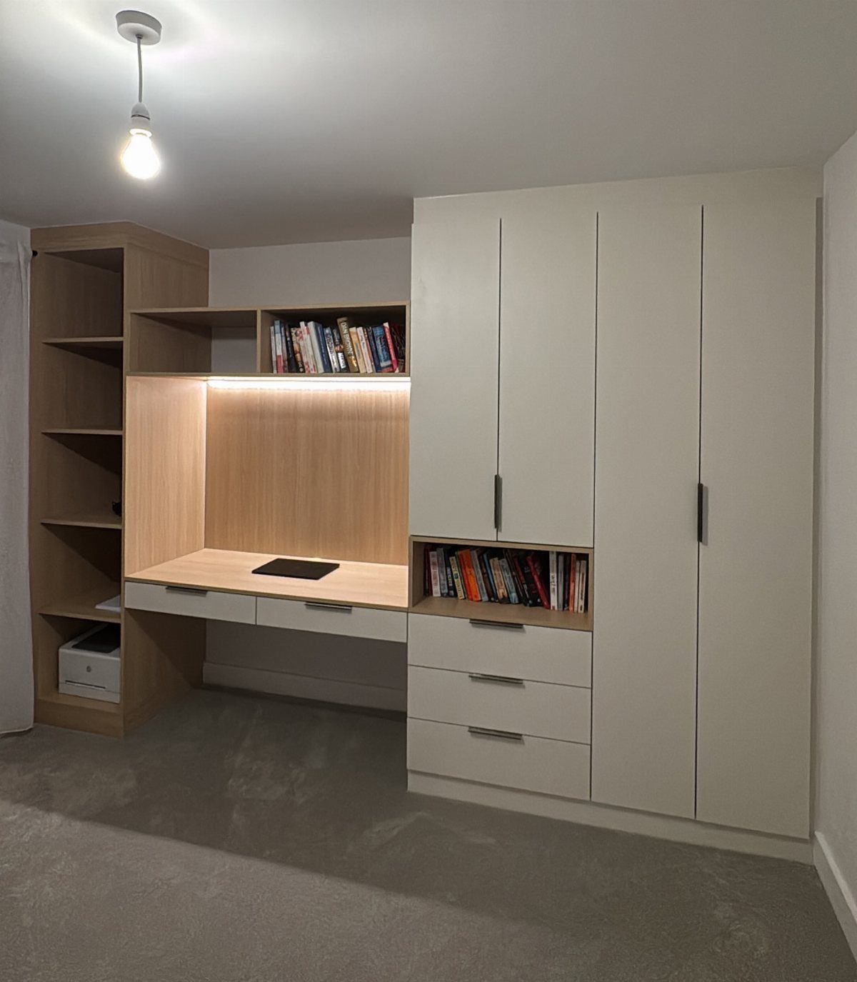 Built-in desk with light wood finish and open shelves above it holding books.