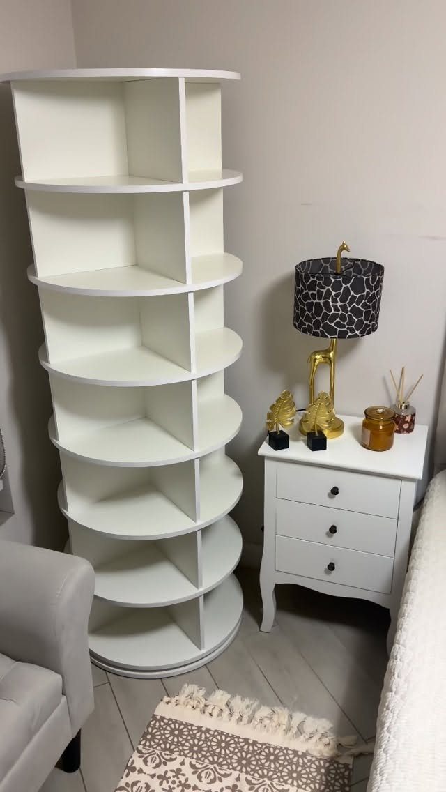 White spiral bookshelf standing next to a white nightstand in a bedroom setting
