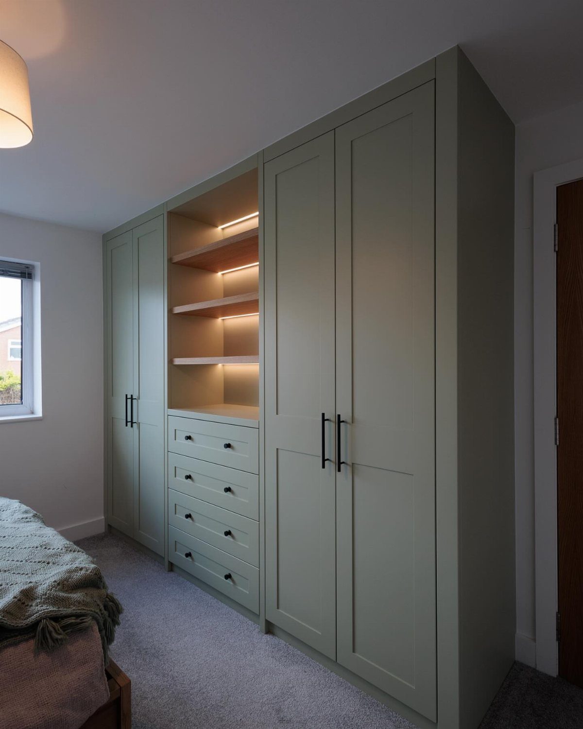 Sage green wall-to-wall closet with integrated wooden shelves and drawers in a bedroom.