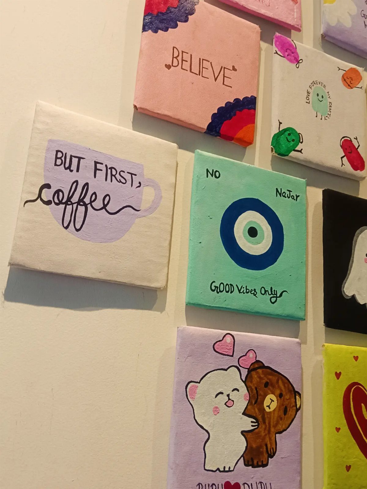 Small square canvas paintings with colorful art and quotes hanging on a white wall.