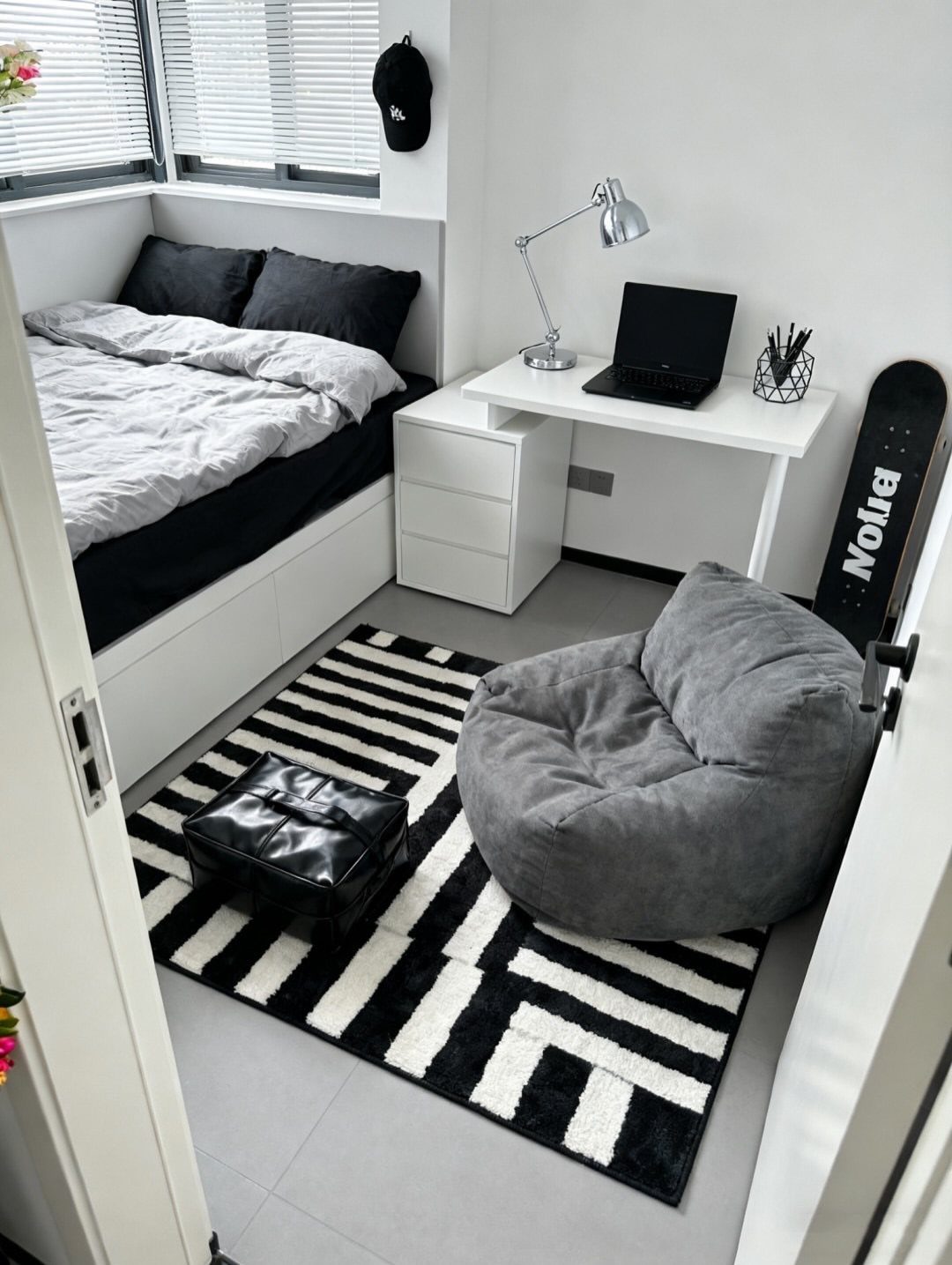 Small bedroom and office combo with white furniture, grey bean bag, and geometric rug.