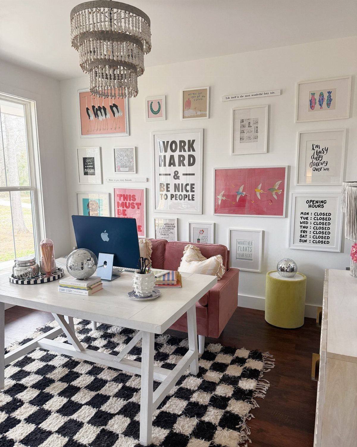 Gallery wall with framed art prints above a white desk and pink sofa.