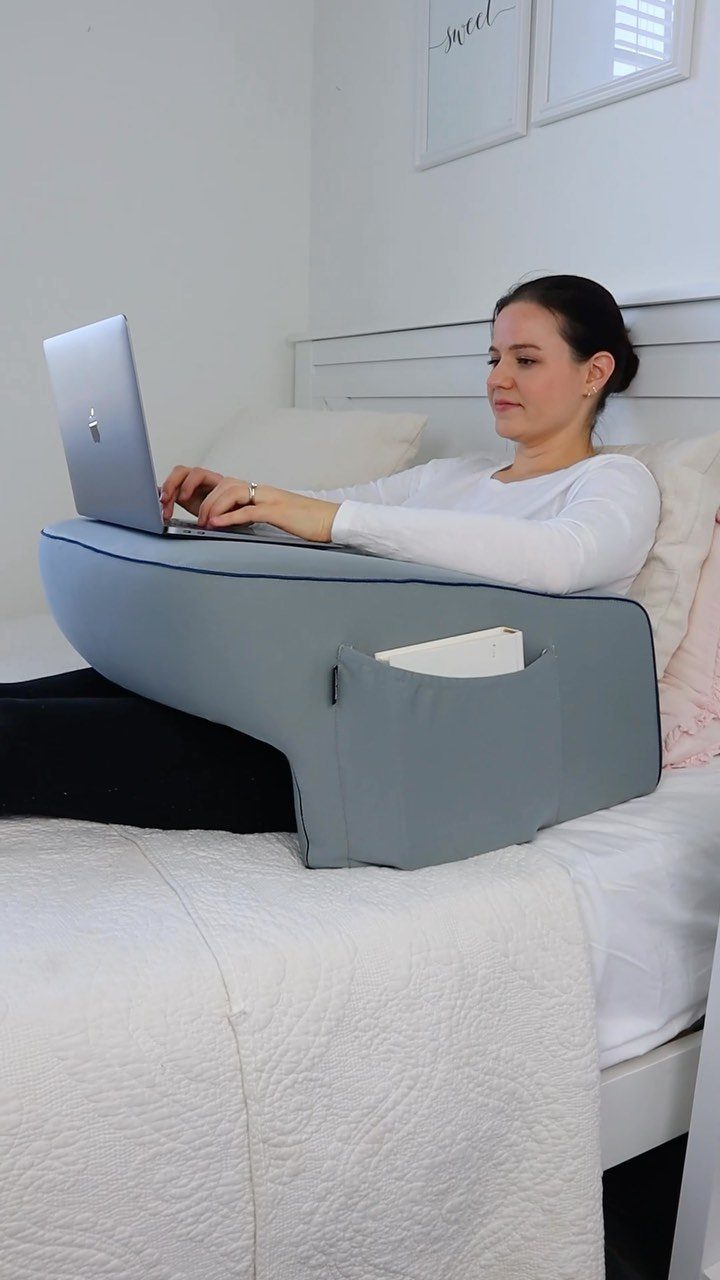 Woman using a laptop on a grey lap desk while sitting in bed