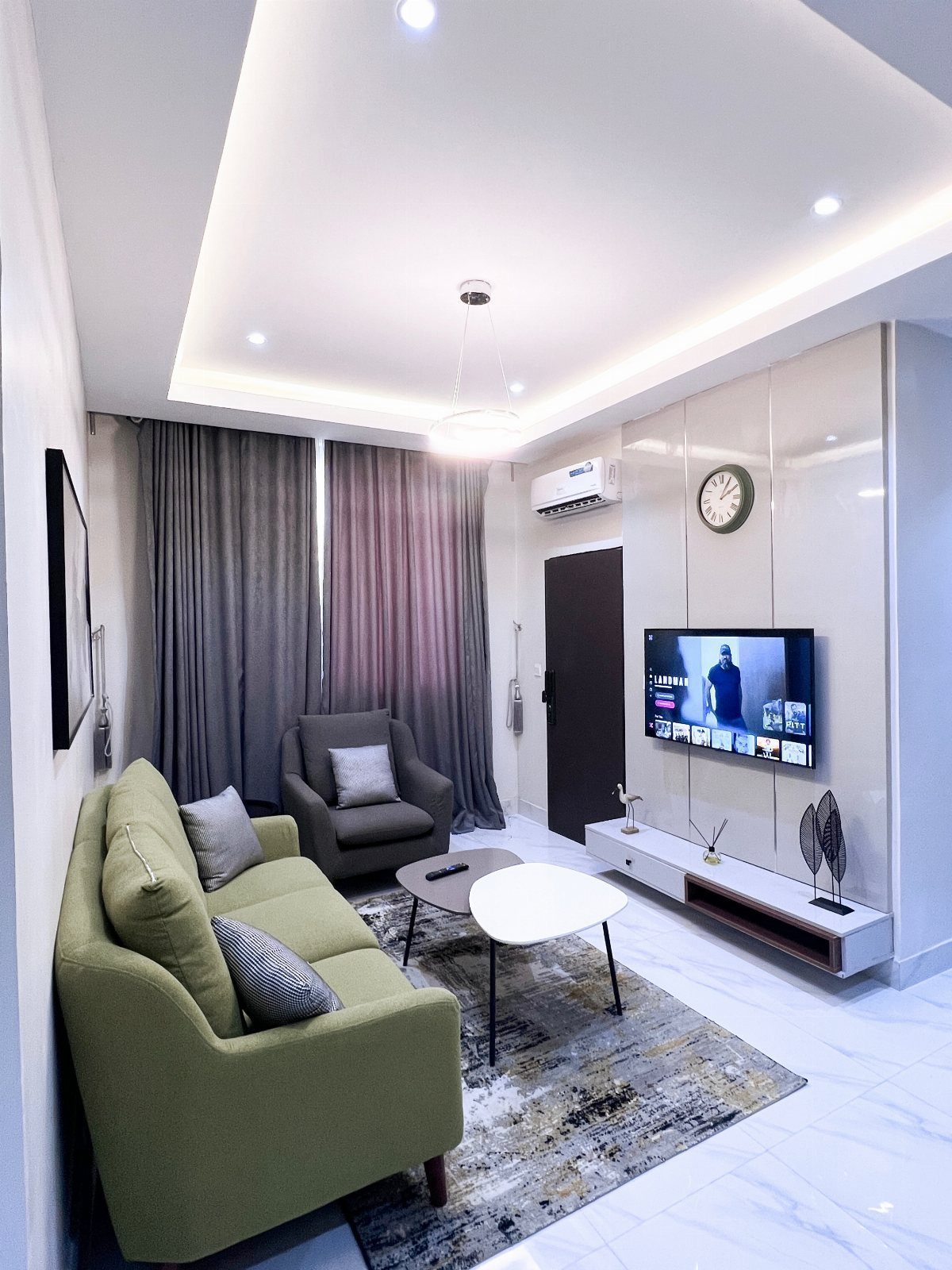 Modern living room with green sofa, grey armchair, and wall-mounted television.