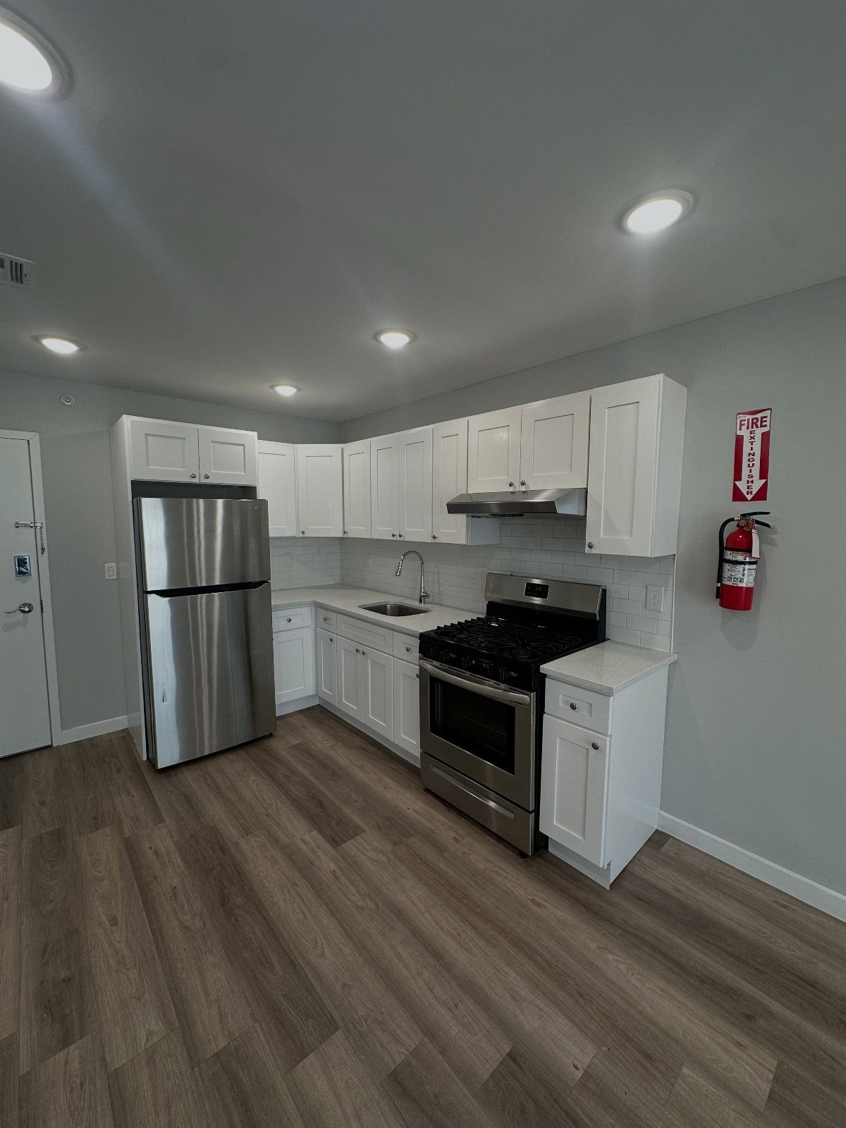 Modern small kitchen with white cabinetry, stainless steel appliances, and grey laminate flooring.