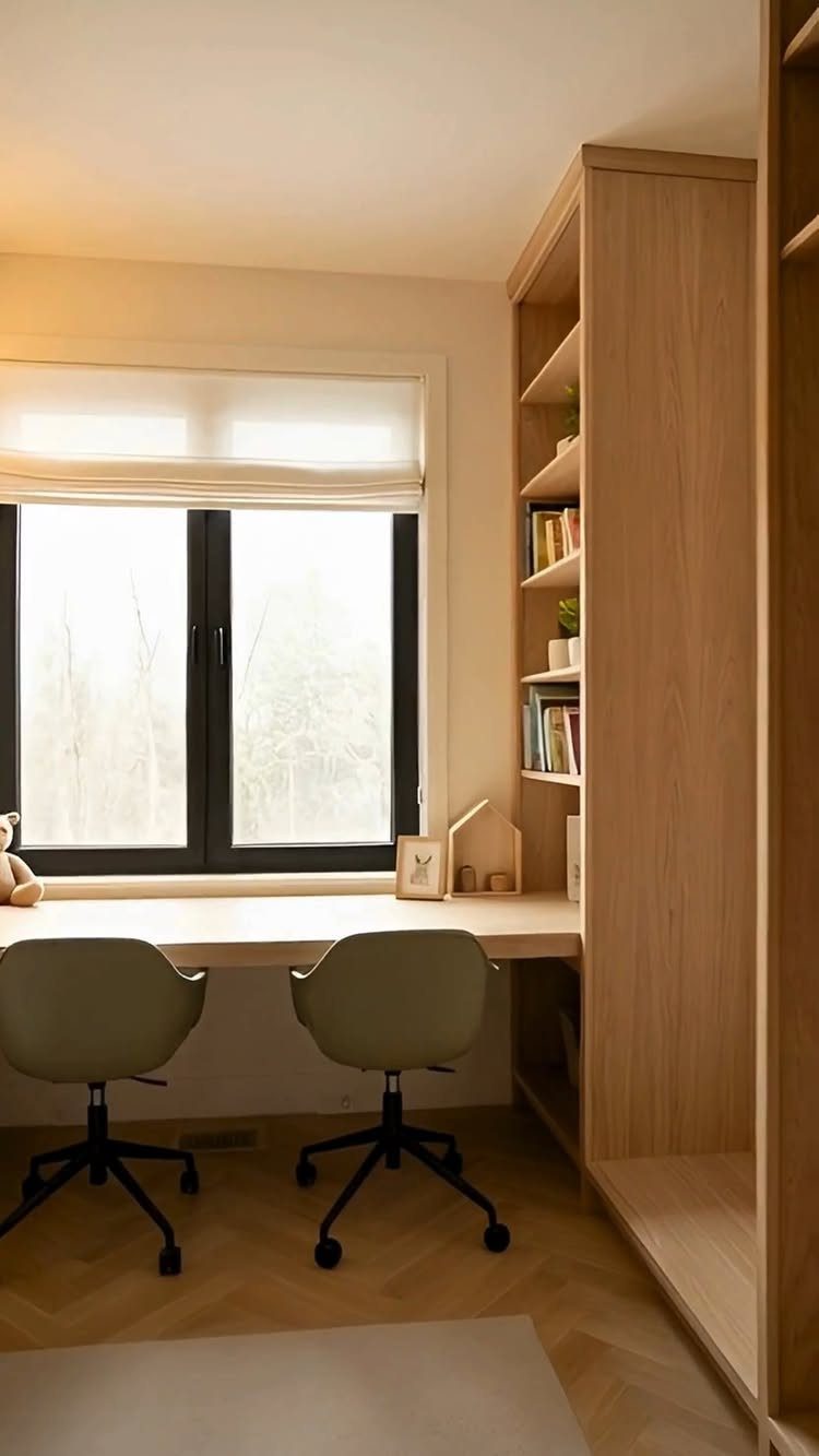 Wooden built-in desk and tall shelving unit with two grey office chairs.