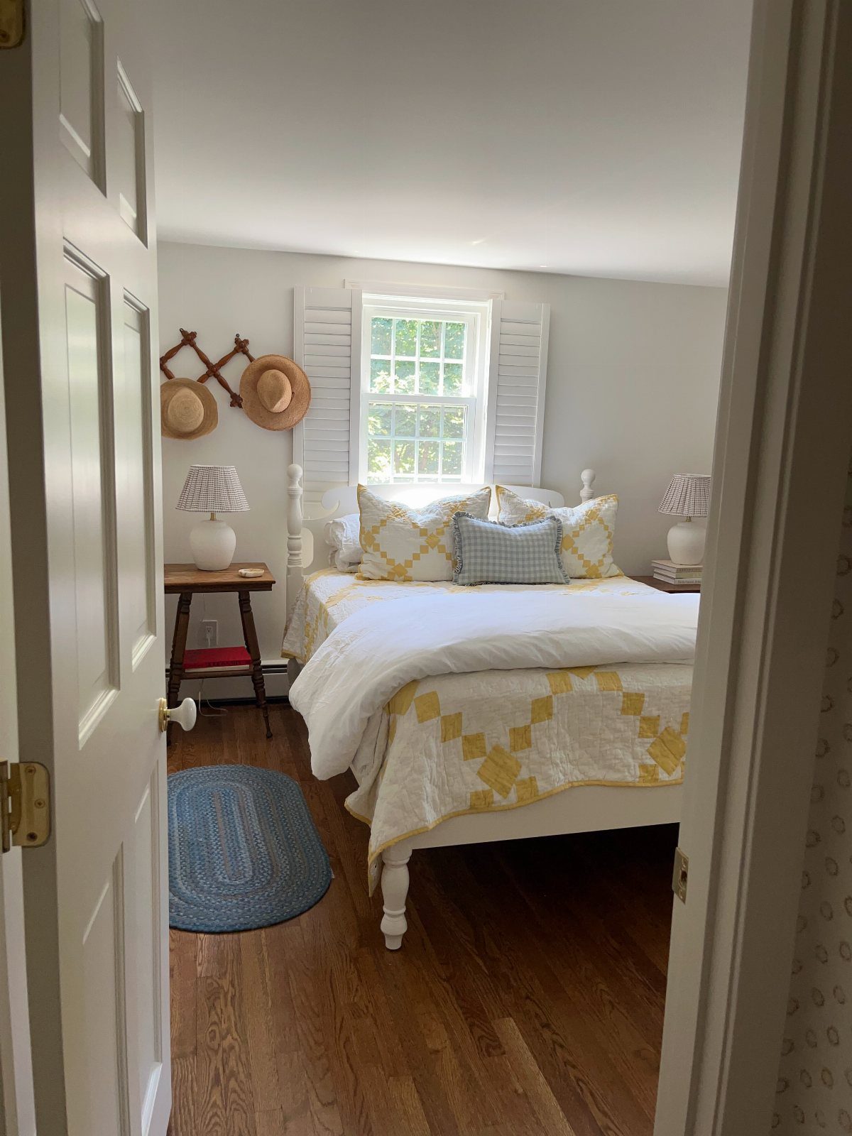 White bed with yellow quilted bedding and decorative pillows in a small bedroom