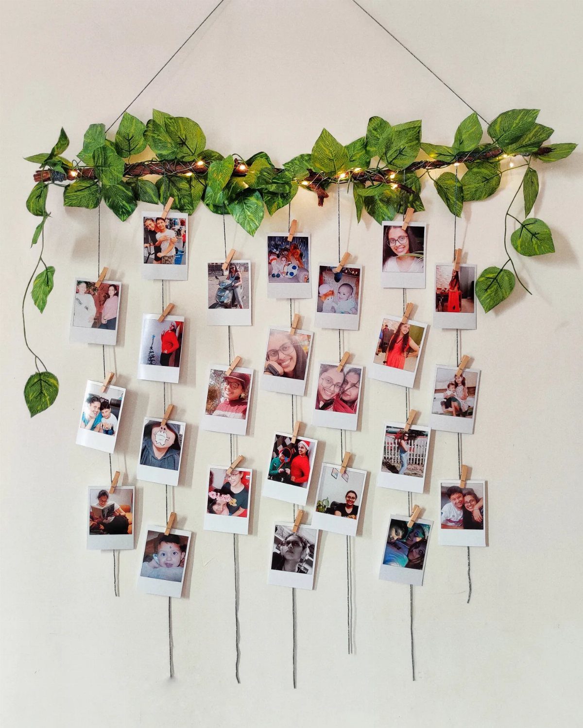 Polaroid photos hanging from a leafy branch with fairy lights on a white wall