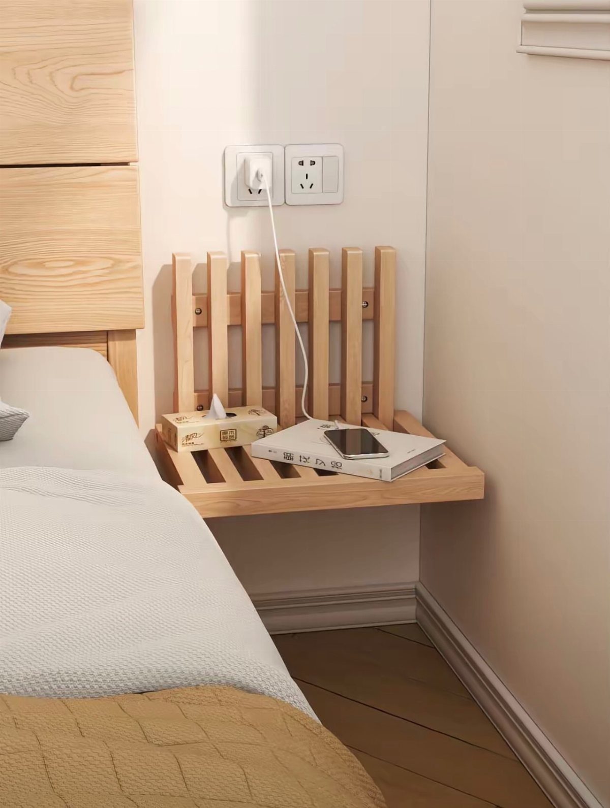 Wooden floating bedside shelf with a phone and book next to a bed