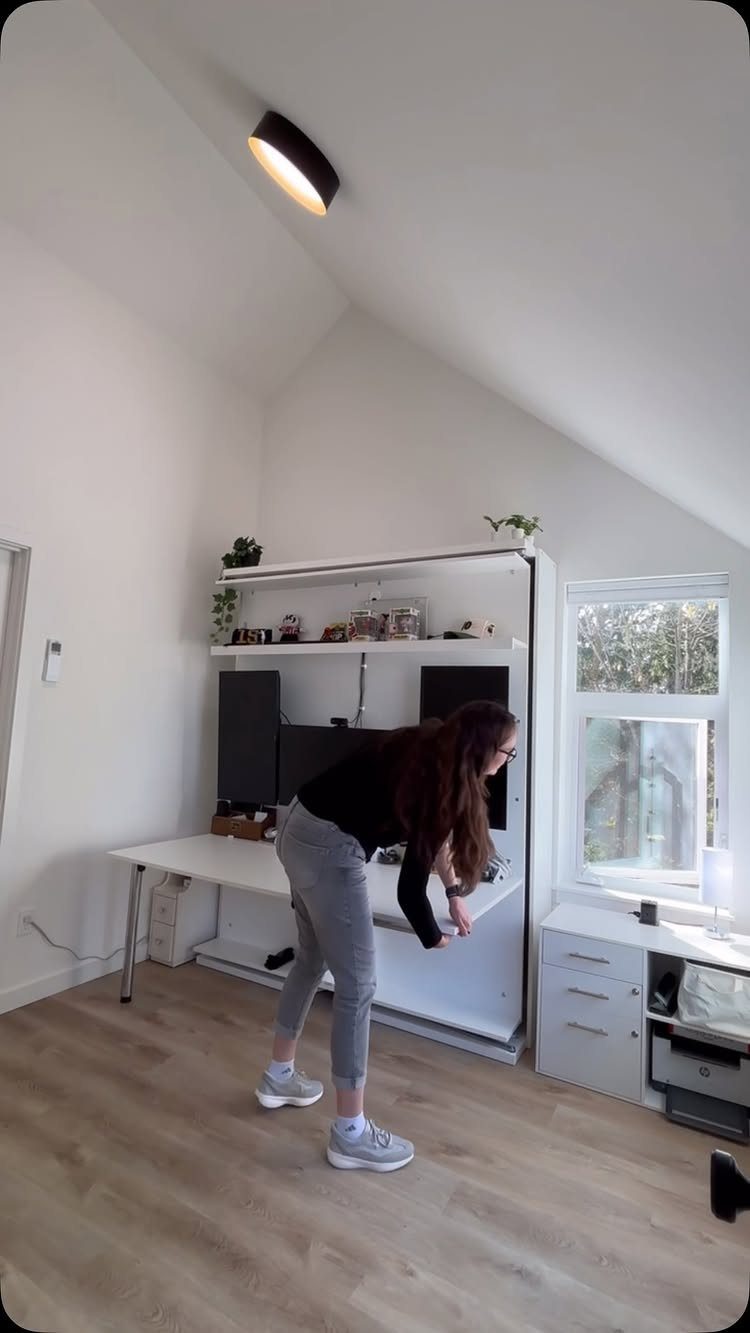Woman adjusting a white Murphy bed and desk combination in a small room.