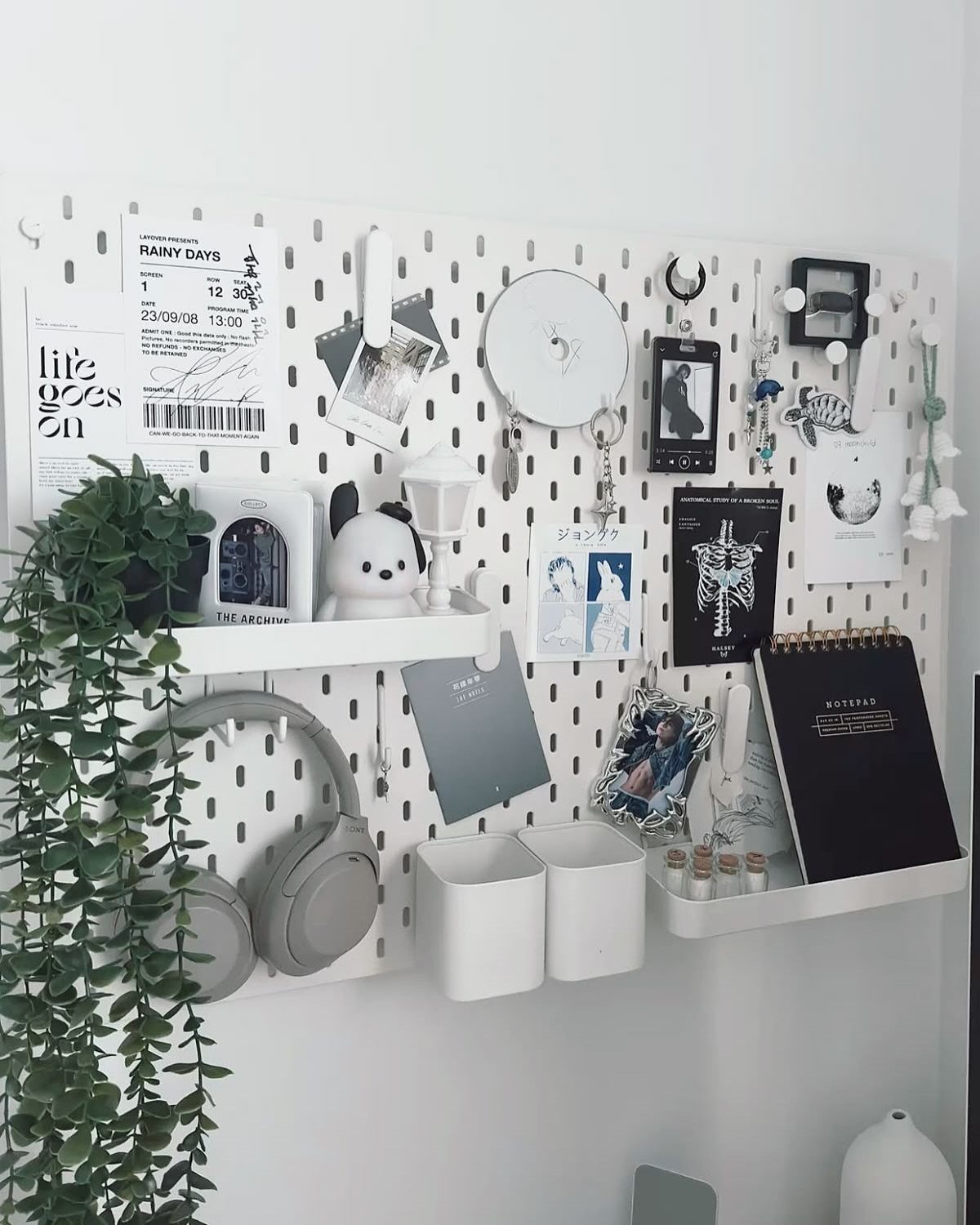 White pegboard organizer on a wall with headphones, photos, and small shelves.