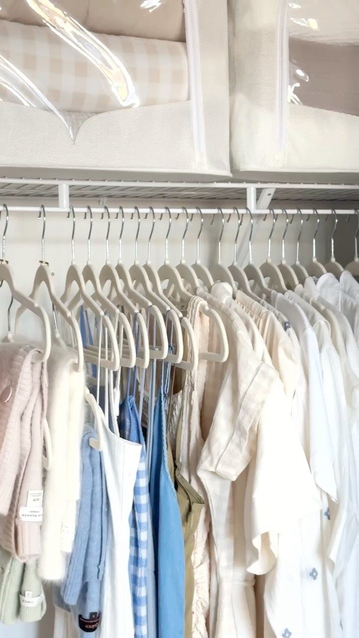 Slim white hangers holding light-colored clothing on a white closet rod.