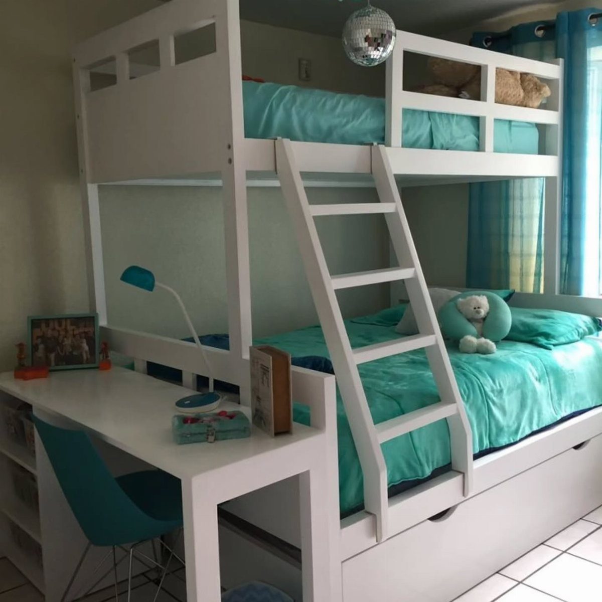 White wooden bunk bed with turquoise bedding and an attached white study desk.