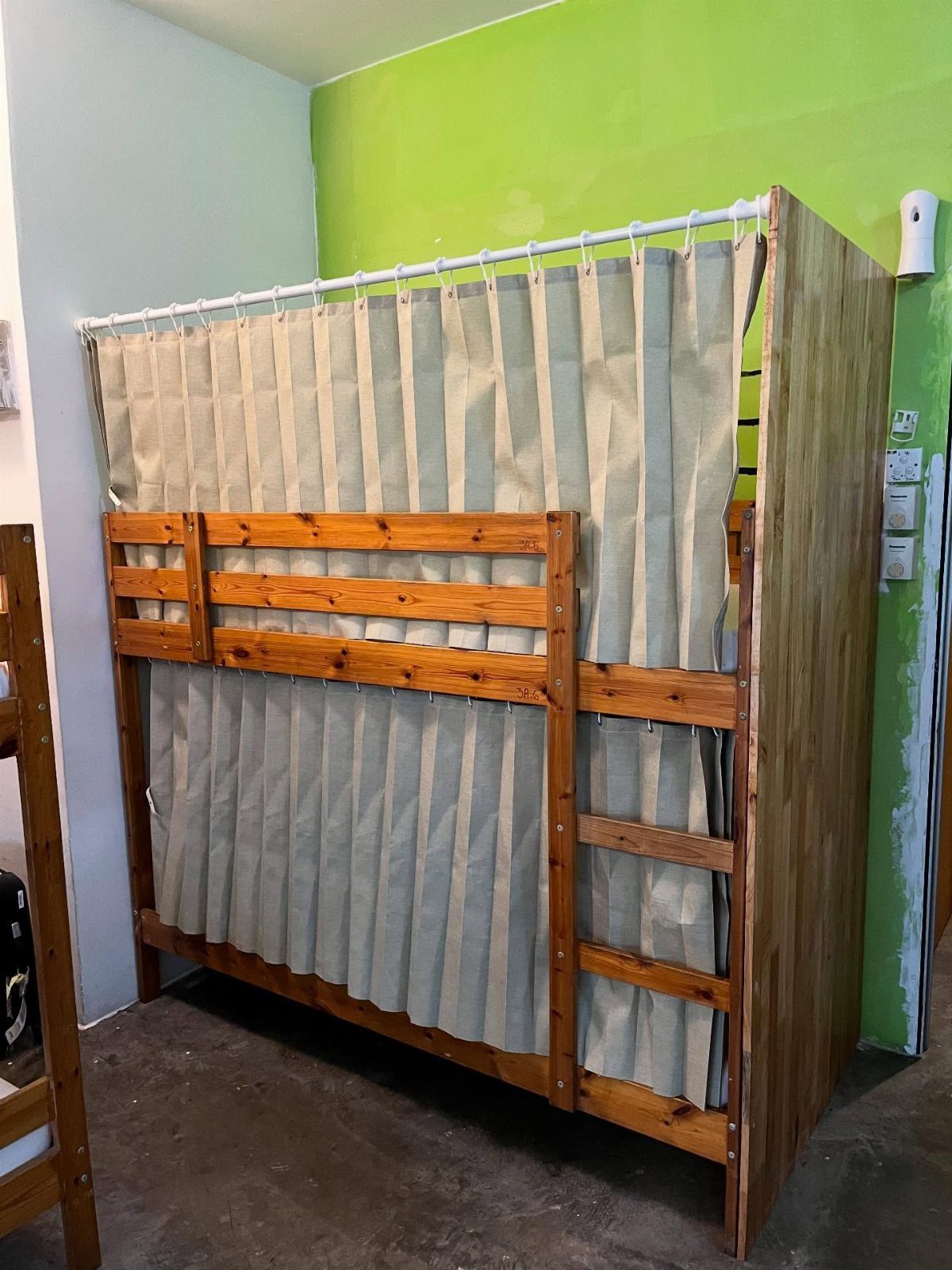 Wooden bunk bed with beige privacy curtains against a lime green wall.