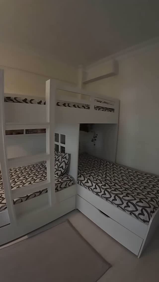 White L-shaped bunk beds with black and white patterned bedding in a small room.