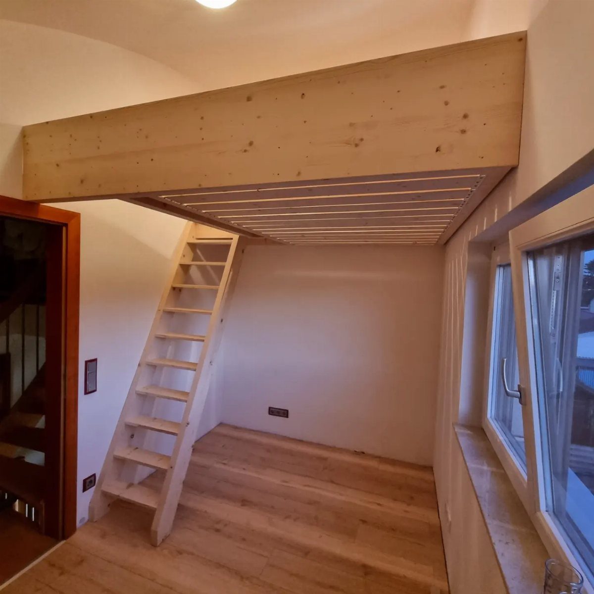 Wooden loft bed with a ladder and open space underneath in a bright room.