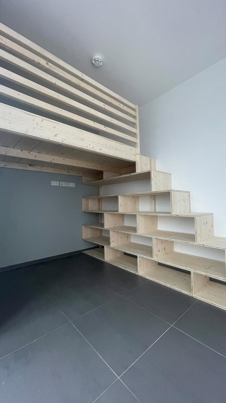 Wooden loft bed structure with built-in shelving stairs in a modern room.