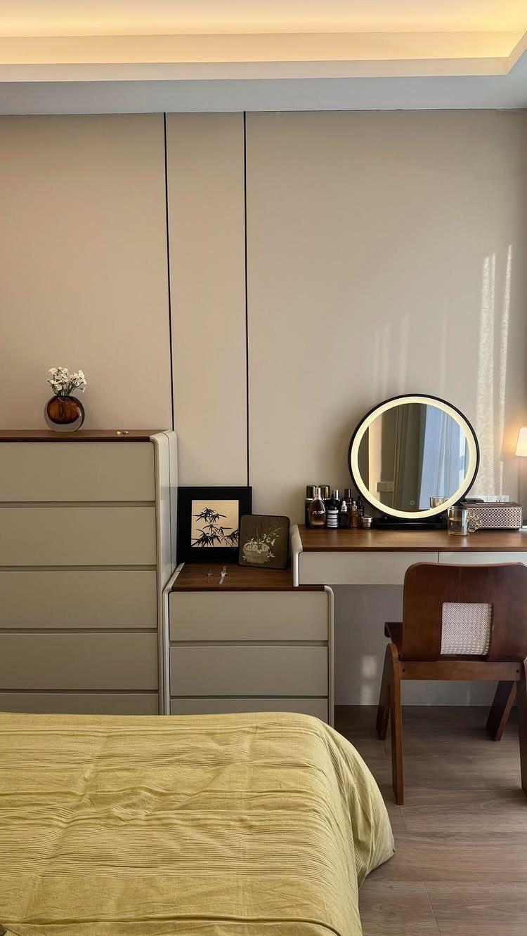 Light-colored dresser and integrated vanity desk with round mirror in a neutral bedroom.