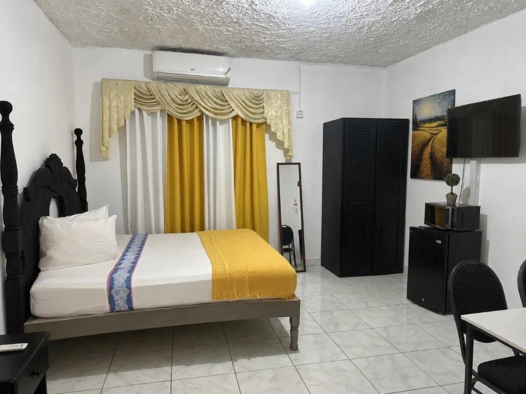 Bedroom with yellow and white bedding, matching curtains, and black furniture on white tiles.