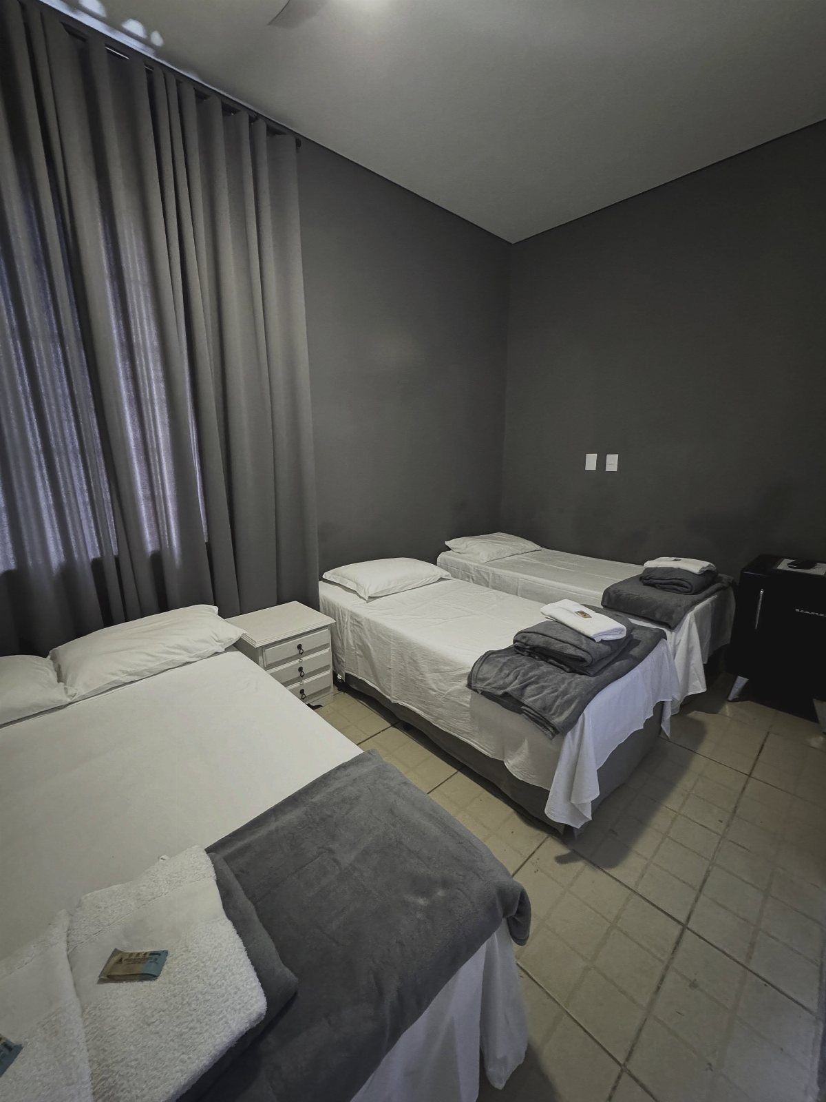 Three single beds with white linens and grey runners in a grey bedroom.
