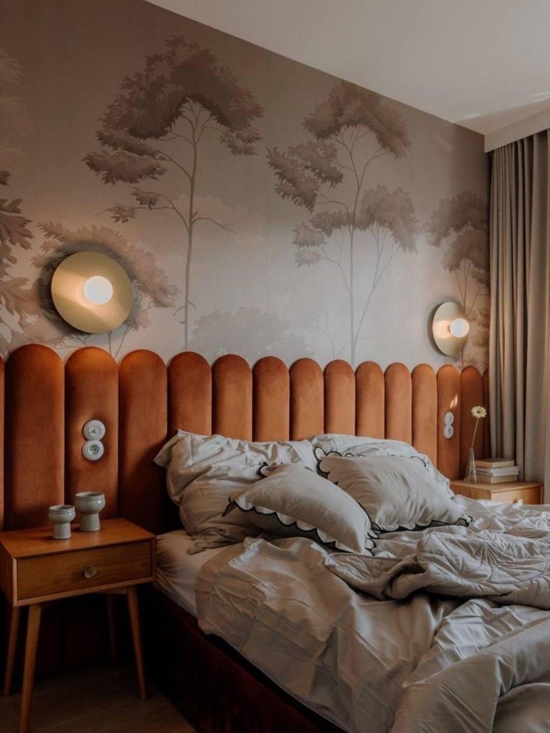 Orange velvet scalloped headboard against a grey tree-patterned wallpaper in a bedroom.