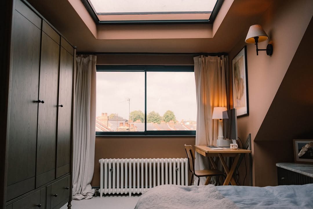 Attic bedroom with brown walls, a skylight, wooden desk, and dark grey wardrobe.