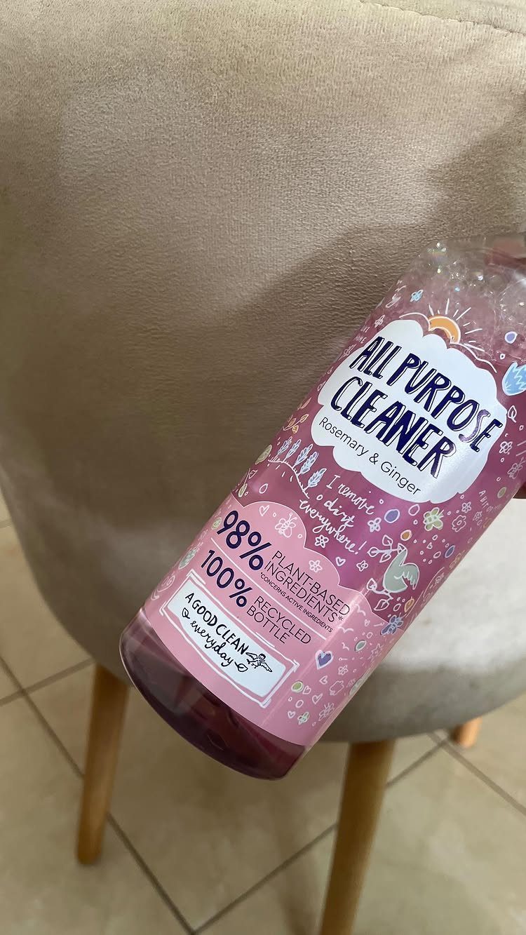 Pink all-purpose cleaner bottle resting on a beige fabric chair with wooden legs.