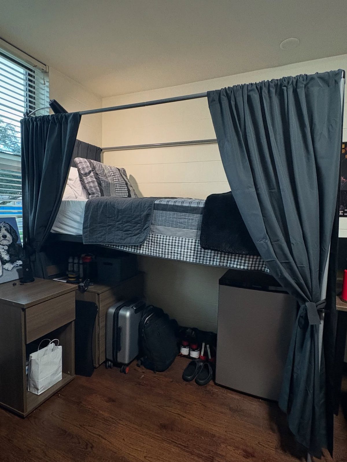 Grey curtains hanging around a lofted dorm bed with storage underneath.