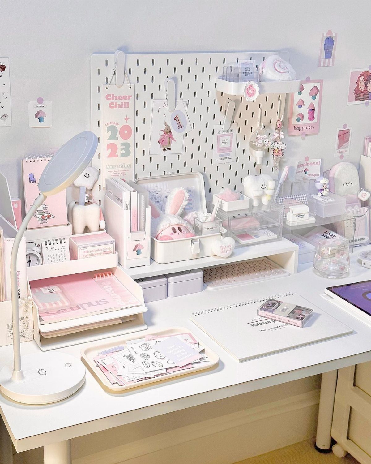 White desk setup with a pegboard, lamp, and pink stationery organizers for studying.