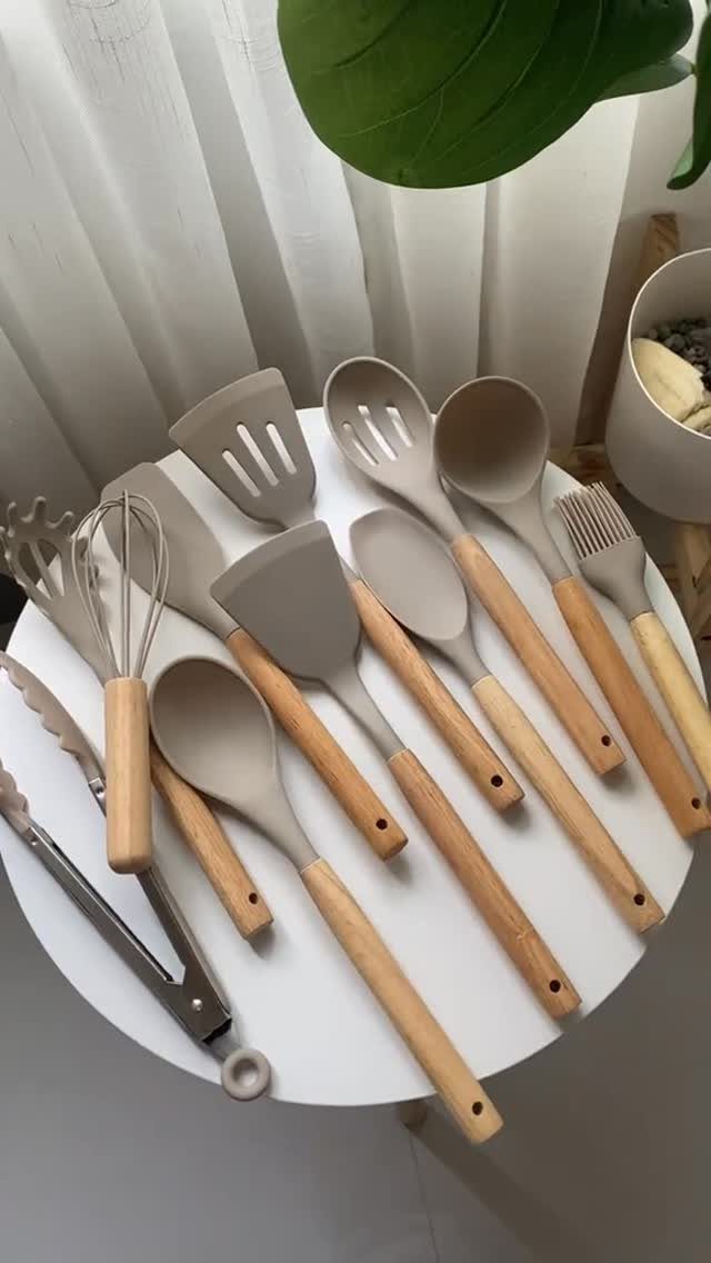 Beige silicone kitchen utensils with wooden handles arranged on a white round table.