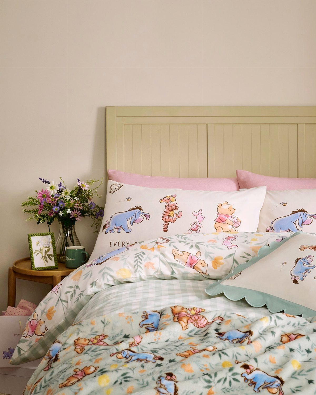 Winnie the Pooh themed bedding and pillows on a bed with green headboard.