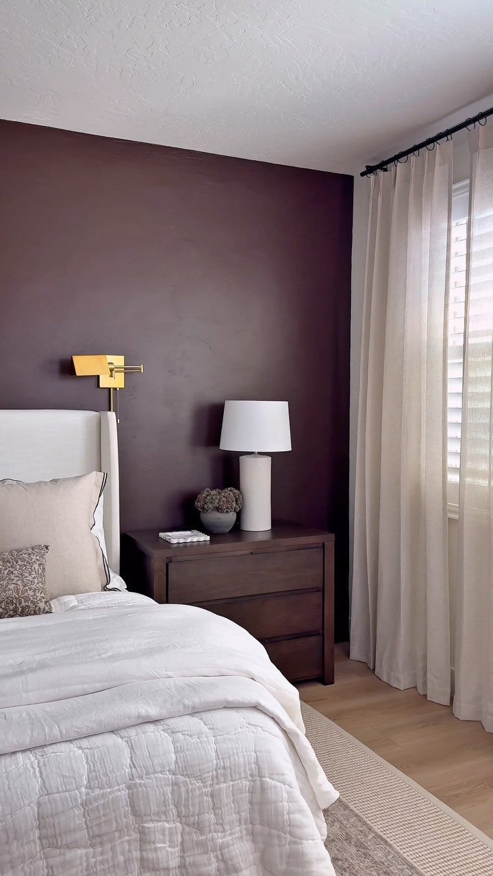 Dark purple accent wall in a bedroom with white bedding and white curtains.