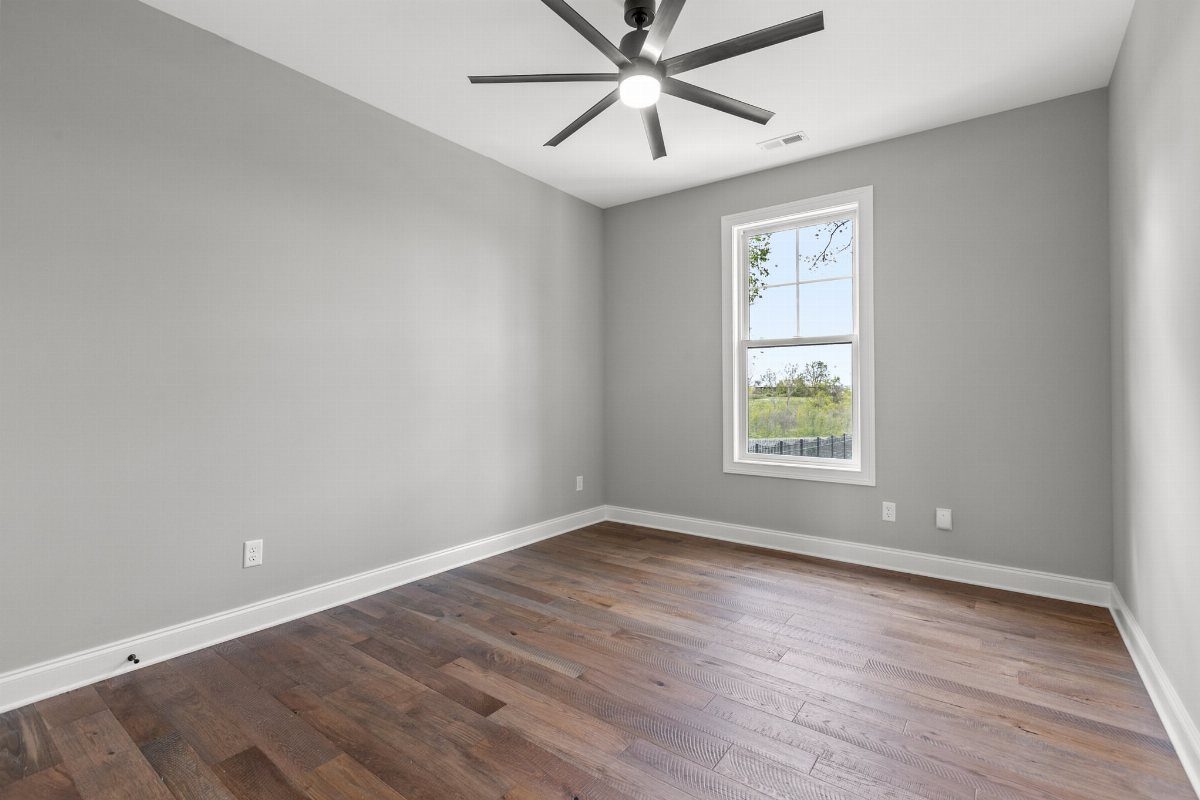 Pale gray walls in an empty room with dark hardwood floors and ceiling fan.