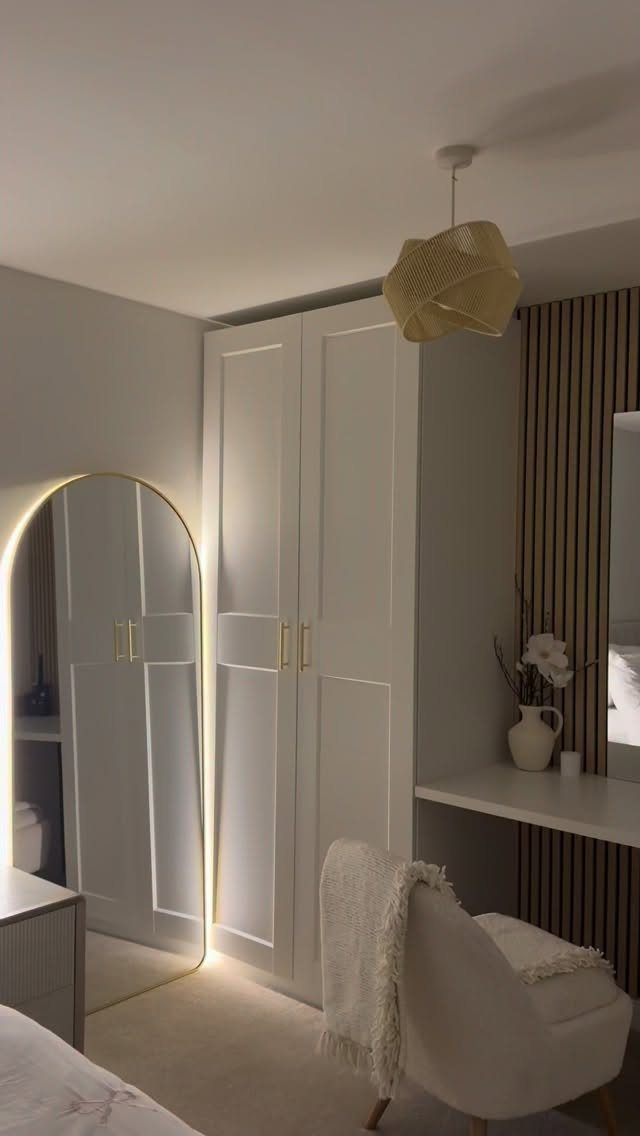 Off-white bedroom walls with a white wardrobe, arched mirror, and white armchair.
