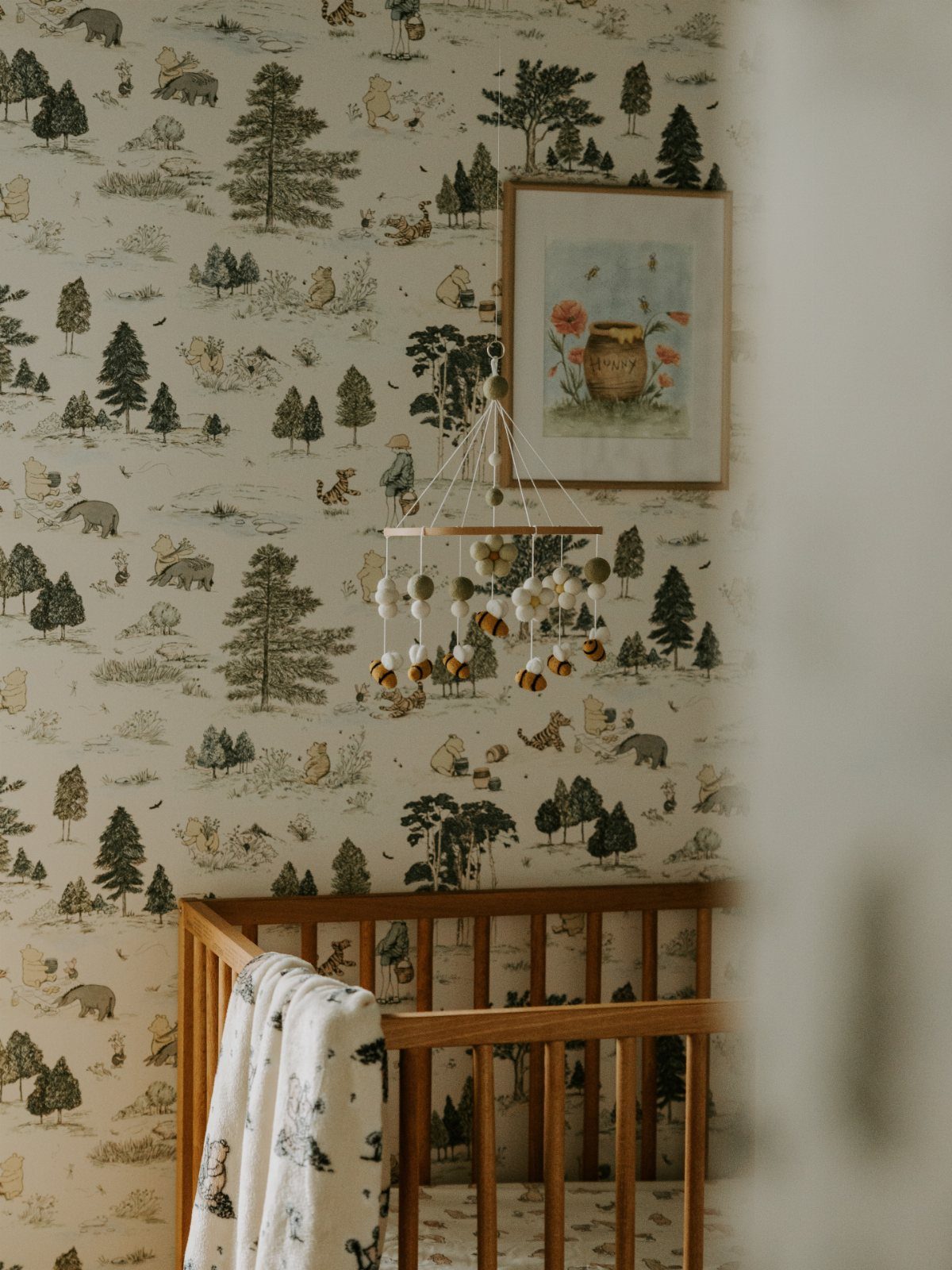 Winnie the Pooh nursery with themed wallpaper, wooden crib, and honey pot mobile.